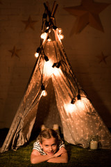Carefree kid lying in wigwam with bulbs in dark room © LIGHTFIELD STUDIOS
