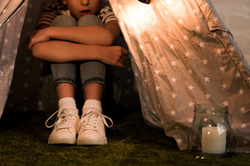 Cropped view of kid sitting in wigwam and embracing knees © LIGHTFIELD STUDIOS