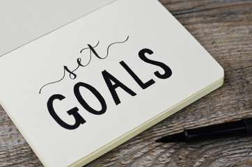 SET GOALS hand lettering in notebook with pen on wooden background