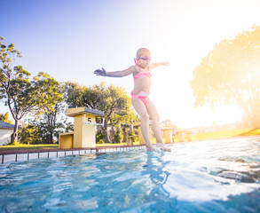 Wide angle view as a young girl jumps into a swimming pool