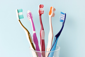 Multicolored toothbrushes in a glass cup front view, blue background