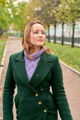 Portrait of a natural blue-eyed woman model in a purple sweater and green coat in the autumn city park.