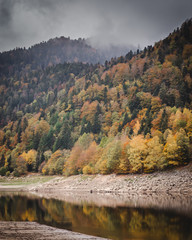 Lake Kruth-Wildestein in Vosges with low waterlevel and autumnal trees on mountains. dark moody skies