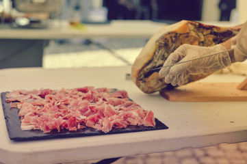 Closeup on person hands slicing carving delicious dry-cured ham prosciutto, prepared delicatessen food culinary background.