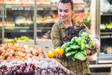 Woman in the supermarket. Beautiful young woman shopping in a supermarket and buying fresh organic vegetables