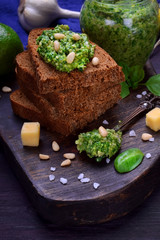 Green pesto in a jar and on a piece of bread surrounded by the ingredients