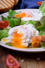 Poached egg with liquid yolk and green salad on a white plate