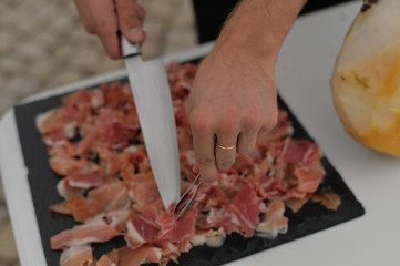 Closeup on person hands slicing carving delicious dry-cured ham prosciutto, prepared delicatessen food culinary background.