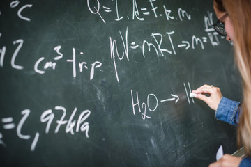 Pretty, young college student writing on the chalkboard/blackboard during a math class (colort toned image; shallow DOF)