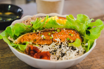 Grilled salmon, rice, white bowl on wooden background, close up view