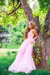 Fototapeta na wymiar A young girl in a pink dress posing in a green botanical garden