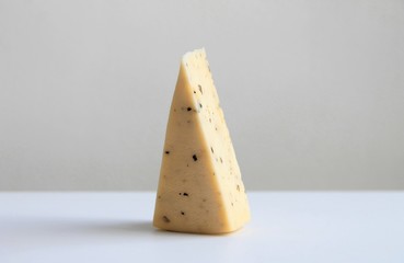 Triangular piece of cheese with herbs is on a white background.