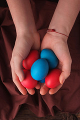 Woman hands hold colored easter eggs on brown cloth background. red and blue eggs. concept of holiday mood.Top view