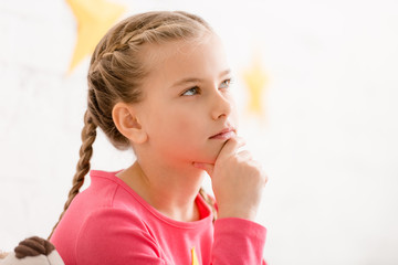 Adorable thoughtful child with braids touching chin