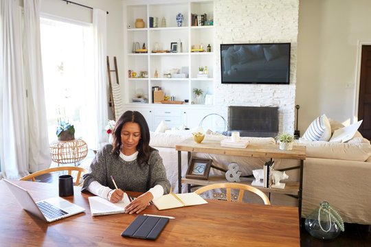 Happy Middle Aged Mixed Race Woman Sitting At Table In Her Dining Room Making Notes, Elevated View