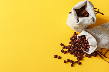 Roasted coffee beans in small sack on yellow background