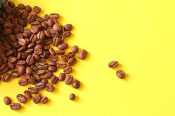 Coffee beans randomly scattered on yellow background.
