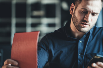 Handsome young man employee sitting at the table and working with notepad and mobile phone