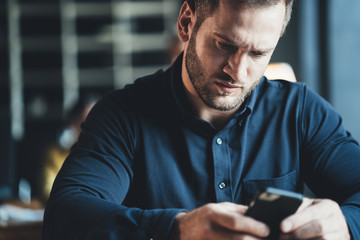 Surprised man employee sitting at the table and working with mobile phone