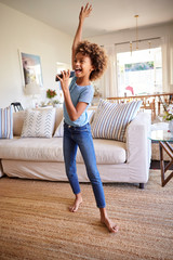 Pre-teen girl dancing and singing in the living room at home using her phone as a microphone, full...