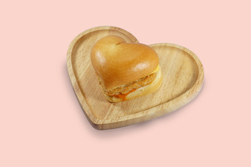 Heart shaped hamburger on wooden plate and pink background.