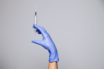 Closeup doctor's hand in rubber latex purple glove hold transparent syringe. Isolated on white...
