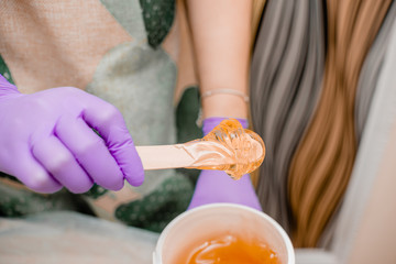 Wax bar with sugar paste depilation and beauty concept - sugar paste or wax honey for hair removing with bright  purple gloves hands of cosmetologist in spa salon. Top view several objects