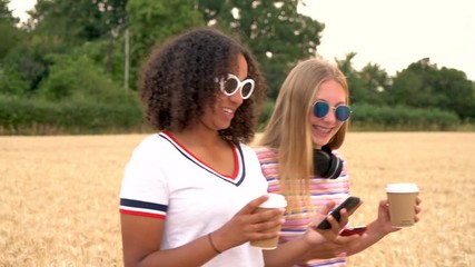 Slow motion video clip of pretty blonde girl and mixed race teenager young women wearing sunglasses drinking coffee and taking selfies on their smart phones 