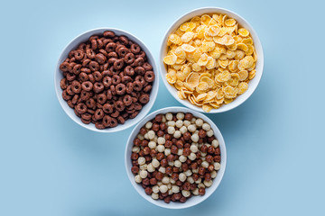 Cereals bowl with chocolate balls, rings and yellow corn flakes for dry breakfast on blue background.