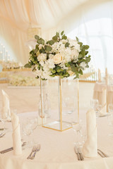 Luxurious glass vase with a bouquet of white flowers on the table in the banquet room during a wedding celebration