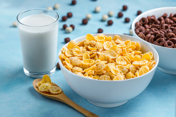 Spoon and bowl with chocolate rings, yellow frosted corn flakes and a glass of milk for dry, cereals breakfast