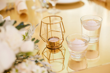 White candles in candlesticks with water on the table in gold color