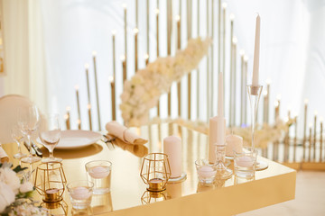 Wedding table for newlyweds of gold color decorated with white candles in candlesticks