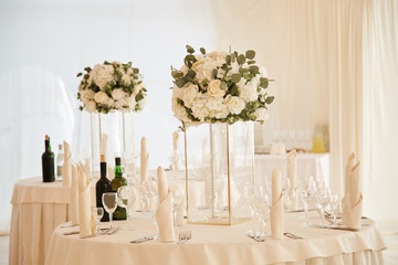 Dining tables during the wedding ceremony are decorated with a white tablecloth and bouquets of flowers in glass vases.