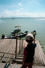 View of a kids watching a man tie a rope to secure his boat to a wooden jetty. view from a wooden jetty