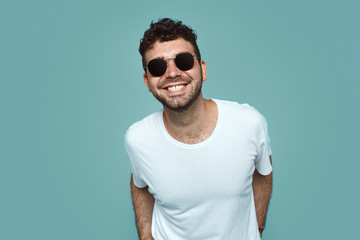 Headshot of satisfied cheerful handsome man grins at camera, isolated over blue studio background. People, positive emotions and facial expressions concept