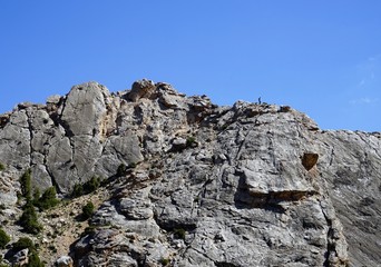A steep rock mountain and blue sky, man just visible walking on the top, Fann Mountains, Tajikistan 