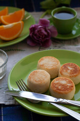Delicious Dietary Cheesecakes from Homemade Farmer's Cheese for breakfast, black coffee in a green cup, chopped orange and.and purple tulip on a blue tablecloth