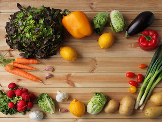 Food background. Fresh organic raw carrots, lettuce, paprika, lemons, eggplant, radishes, potatoes, tomatoes, vegetables on a light wooden background, shot from the top with place for text
