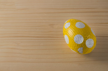an easter chocolate egg wrapped in yellow paper with white polka dots, isolated on wood