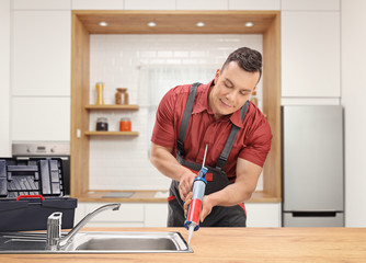 Plumber using a silicone tube on a sink inside a modern kitchen