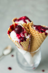 Vanilla ice cream in a waffle cone in a glass with berry sauce