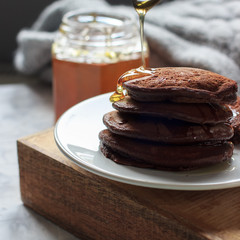 Chocolate pancakes with honey on a wooden tray on grey background