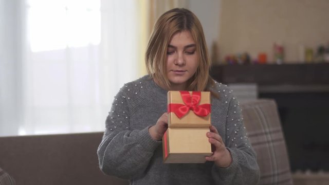 Portrait of happy joyful bbw opening gift sitting on sofa in room