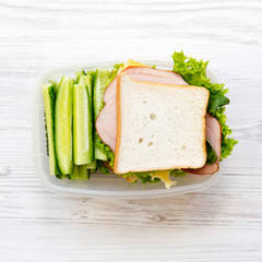 Lunch box with sandwich and vegetables on white wooden surface, top view. Flat lay. From above.