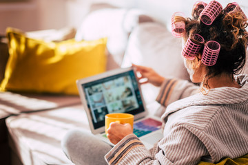 Housewife at home with curlers on his head waiting the time watching a movie on the tablet - woman using technology at home while getting beauty - wellness and lifestyle concept for girls
