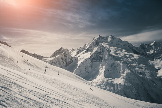 Wide ski piste and chair ski lift on the background of the beautiful Caucasus Mountains and the bright sun