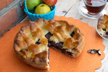 pie, a piece of apple pie with cherry and walnuts, a cup of tea, apples in a basket and walnuts on...