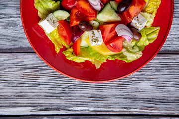 Greek salad of fresh cucumber, tomato, sweet pepper, lettuce, red onion, feta cheese and olives with olive oil on wooden background. Healthy food