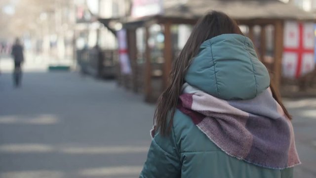 Slender girl in anorak and scarf walking along a street in winter in slo-mo  